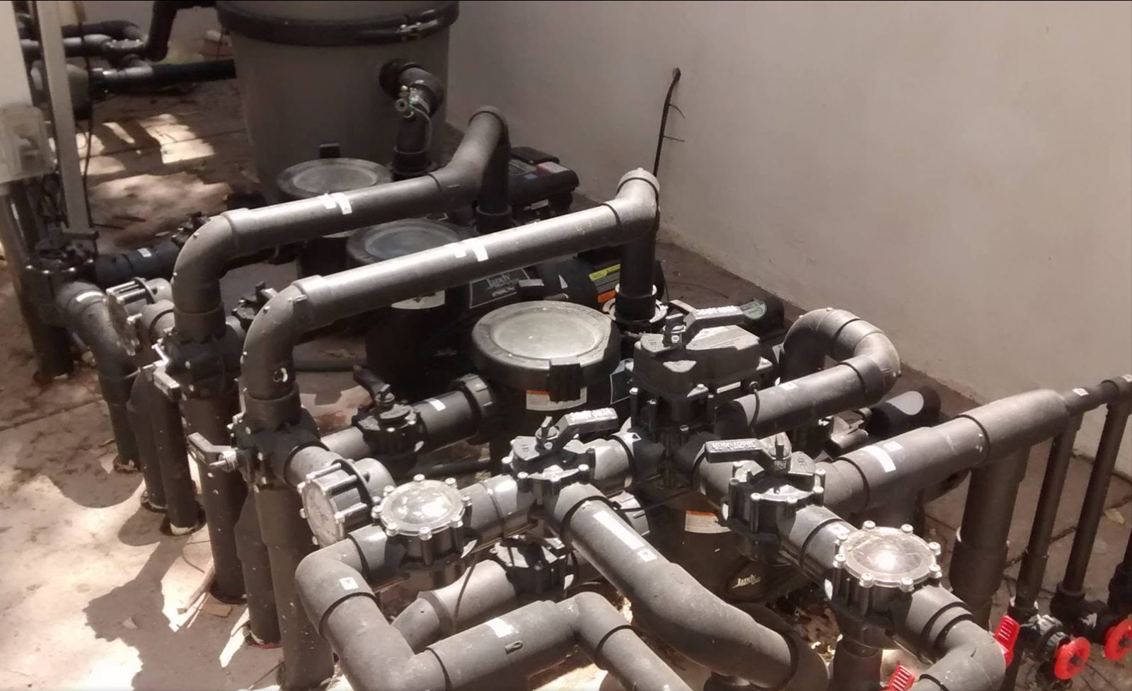 Pool equipment pad with pumps, filter, and black PVC plumbing