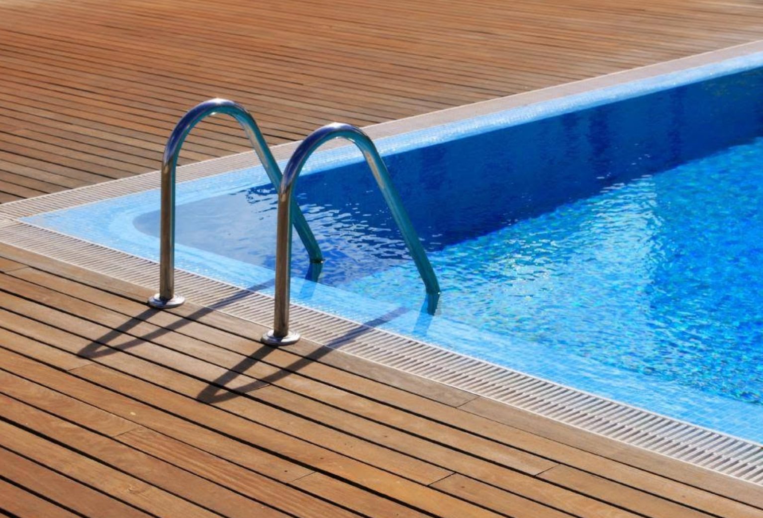Pool ladder on a wood deck beside clear blue water